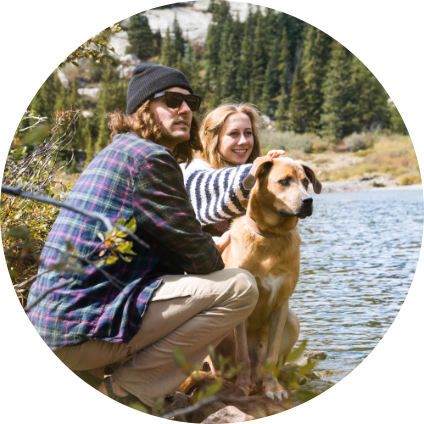 Deux personnes avec un chien au bord d'un lac.